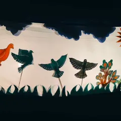 A beautiful close-up of the hand-painted leather puppets depicting a flock of birds. The intricate details and vibrant colors of the Chitrakathi art form are visible even in silhouette.