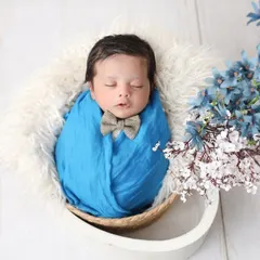 A dapper little gentleman. Swaddled in blue with a tiny bow tie, this baby boy looks perfectly peaceful, complemented by delicate blue and white flowers.