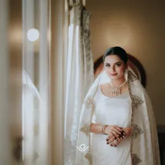 An elegant Muslim bride in a white and gold ensemble, her portrait taken by a window to capture a serene and timeless look.