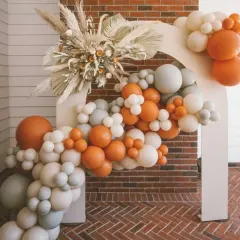 This modern-boho balloon arch combines earthy orange and muted grey balloons with a large arrangement of dried pampas grass and palm leaves. The double-arch backdrop adds a contemporary architectural element to the design.