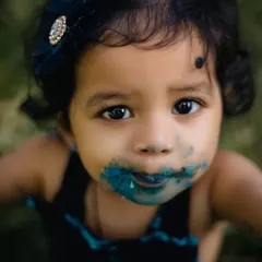 A joyful and messy close-up of a one-year-old's face, delightfully covered in blue cake frosting during her first birthday cake smash. This captures the pure, uninhibited fun of celebrating childhood milestones.