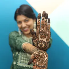 A creative shot focusing on the detailed bridal henna, with the bride's smiling face softly blurred in the background. This technique highlights the artistry of the mehandi.