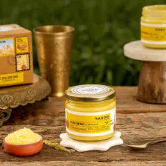 A styled shot of Barosi's cow ghee on a rustic wooden table. The composition with traditional brassware and a small bowl of ghee emphasizes its purity and traditional value.