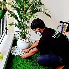 A close-up of my work on a balcony garden. I'm adding decorative white pebbles to a potted Areca palm set on artificial turf, creating a clean and stylish look.