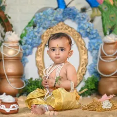 A classic Little Krishna pose. This setup features traditional pots, peacock feathers, and a beautiful arch, creating a perfect backdrop for this baby dressed as Krishna, complete with pearl necklaces.