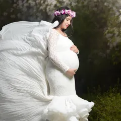 An angelic portrait of a mom-to-be in a white lace gown with a dramatic flowing train. The soft, natural setting and floral crown complete this ethereal maternity look.