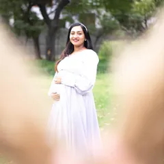 This is a creative and heartfelt shot, framed by the father-to-be's hands making a heart shape. It beautifully centers the expecting mother and her bump, symbolizing that she is the heart of their growing family.