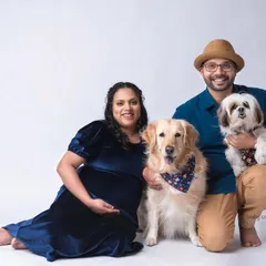 A happy family portrait featuring the expecting couple and their two dogs, a golden retriever and a shih tzu. This studio shot captures the joy and excitement of the entire family, including the furry members, as they await their new arrival.