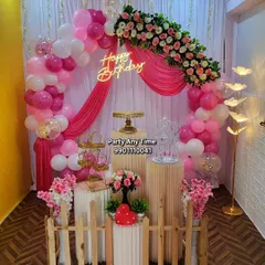 A vibrant pink floral and balloon arch decoration in my party hall, featuring a small picket fence and elegant plinths.