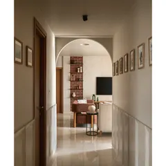 Looking from the corridor back towards the living area, an archway frames the view of the exposed brick wall. The walls of the passage are lined with the family's travel photos, turning a simple hallway into a personal gallery.