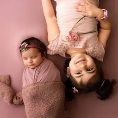 An older sister lies next to her sleeping newborn sibling, a tender moment captured during a newborn session.