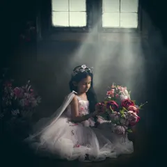 This is an example of our painterly portrait style, where we use dramatic lighting to create a soulful, artistic image. The soft light from the window illuminates this young girl in her princess gown, transforming a simple moment into a timeless piece of art.