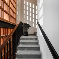 The brick jaali screen seen from the interior stairwell. Throughout the day, sunlight filters through the perforations, casting a dynamic pattern of light and shadow onto the white walls.