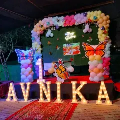 For a truly grand first birthday, I can bring any theme to life. This butterfly garden theme for Avnika's party included a lush balloon arch, a green backdrop, and large, lit-up marquee letters spelling her name, creating a magical photo opportunity.