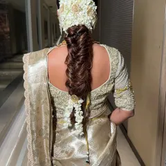 The complete look of the South Indian bridal braid, showing how it elegantly drapes down the back over a golden silk saree. This hairstyle is a statement piece, perfect for a grand wedding ceremony.