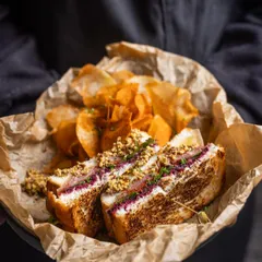 A delightful Ham and Cheese sandwich, perfectly grilled and served with a side of house-made chips. It’s a classic done right, ideal for a satisfying and delicious breakfast.