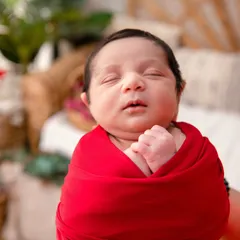 A close-up portrait of a newborn's face, wrapped in a bold red swaddle. This shot emphasizes the baby's peaceful expression and perfect features, using a strong color to create a striking and memorable image.