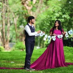 A dad-to-be dressed in a smart navy blue vest and trousers, coordinating perfectly with his partner's magenta gown for their baby shower shoot.