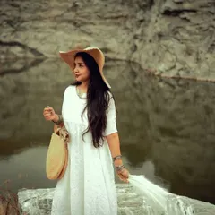 A fashion-forward portrait of a woman in a flowing white dress against a dramatic rock and water backdrop. This image is perfect for a portfolio that aims to blend style with nature.