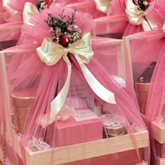 A closer look at our popular pink-themed hamper. A rustic wooden crate filled with goodies is enveloped in soft pink tulle, tied with a cream ribbon, and adorned with a small bouquet of dried flowers.