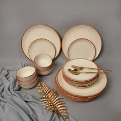 A complete cream-colored, speckled ceramic dinnerware set, elegantly arranged with a golden leaf prop and grey fabric.