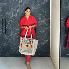 Here is a full view of the pom-pom tote paired with a bright red kurta. The colorful tassels and mirror work add a playful, bohemian touch to the traditional outfit.