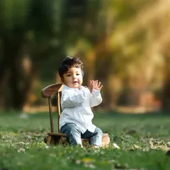 A simple and timeless outdoor portrait of a toddler sitting on a small wooden chair in a sunlit park.