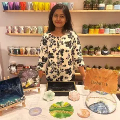 A student displays a variety of her finished resin art pieces, including coasters, trays, and a personalized nameplate, showing the versatility of the medium.