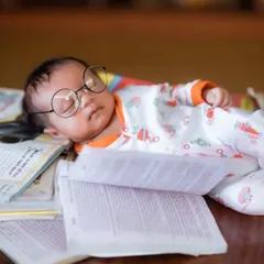 A tiny scholar, dreaming among the books. This close-up captures the serene expression of a sleeping newborn during a themed photoshoot.