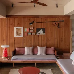 The living room features a floating U-shaped seating arrangement that extends from the raised deck. The continuous use of teak wood on vertical surfaces helps dissolve boundaries and makes the entire space feel more expansive.