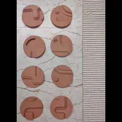 A work-in-progress shot of a set of circular terracotta wall art pieces. Each disc is carved with unique minimalist lines and shapes, creating a collection of small, sculptural artworks.