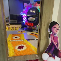 The entrance to a home decorated for a 'Welcome Baby' celebration, featuring a flower rangoli path and a character cutout.