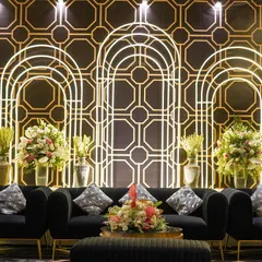 A chic lounge area designed with modern black sofas set against a geometric, art-deco-inspired backdrop. The glowing arches and fresh flowers added softness and elegance.