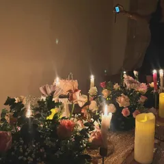This image captures the warm, candlelit ambiance of an 18th birthday celebration. The focus is on the floral sit down table arrangement, with a birthday cake visible in the background, creating a cozy and personal atmosphere.