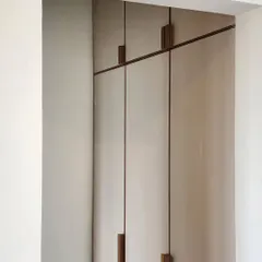 The custom-designed handles on this wardrobe are a study in minimalist detailing. The thin metal rods and simple wooden blocks create a clean, graphic composition against the neutral cabinet doors.