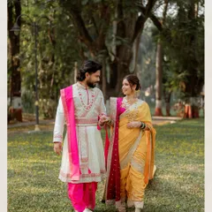 A candid walking shot from a Marathi-themed pre-wedding session. The couple's coordinated outfits, with the groom's white sherwani and pink stole matching the bride's saree, create a visually cohesive and beautiful image.