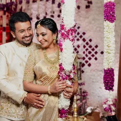 A lovely couple posing amidst floral decor. We designed their matching cream and gold outfits for a traditional ceremony, with intricate gold embroidery on his sherwani and a classic Kanchipuram silk saree for her.