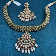 This is a very delicate and pretty kundan necklace set. The design features a crescent-shaped pendant and matching earrings with pearl drops, perfect for someone who wants a traditional but not too heavy look.