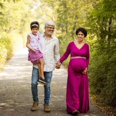 A candid moment during an outdoor family maternity session. The father carries his daughter while holding hands with his expectant wife, capturing the love and movement of this growing family.