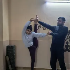 An instructor provides support in Trivikramasana, ensuring the student maintains balance and deepens the stretch safely. This hands-on approach is key to our teaching methodology.