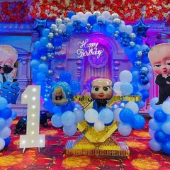 A fun and detailed 'Boss Baby' themed first birthday party. This setup includes custom character cutouts, a large light-up number 'one', and a coordinated blue and silver balloon arch.