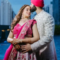 An intimate portrait of a Sikh couple in Bangkok, the groom kissing his bride's forehead with the city's modern skyline and a pool in the background.