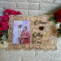 A clear, frontal shot of the frame, highlighting the golden text of the names and wedding date against the backdrop of preserved petals.