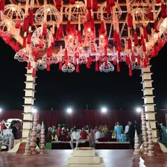 A view from under the magnificent wedding mandap, looking out at the guest seating. The intricate ceiling is covered in red flowers and hanging tassels, creating a luxurious atmosphere.