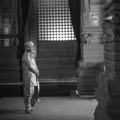 A groom stands in a sliver of light within a dark, cavernous temple hall. This dramatic use of shadow and light creates a moody, contemplative, and powerful black and white portrait.