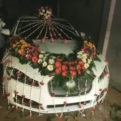 A lavish floral decoration for a white Jaguar, featuring a large arrangement on the hood with strings of flowers cascading down the front.