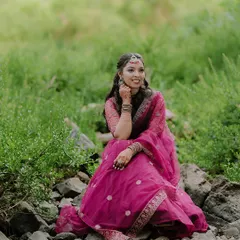 A beautiful solo portrait of the bride-to-be during her pre-wedding shoot, seated on rocks in a lush green landscape.