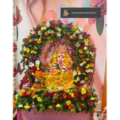 A vibrant and colorful home setup for Ganpati Bappa. The idol is surrounded by a dense arch of multi-colored flowers like marigolds, gerberas, and roses, creating a truly festive and joyous look.