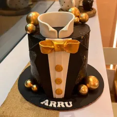 The perfect cake for a gentleman. This tuxedo cake features a sharp black finish with a geometric texture, a fondant collar, a gold bow tie, and elegant gold sphere accents for a sophisticated celebration.