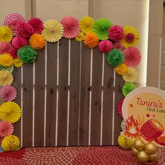 A colorful and festive photo booth for Tanira's First Lohri. The backdrop was made of wooden panels and decorated with vibrant paper fans, with a personalized sign celebrating the milestone.
